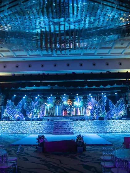 A full view of our modern, iridescent Sangeet stage. The design features a textured, shimmering facade, large-scale abstract leaf structures with integrated lighting, and a massive LED screen backdrop, all coming together to create a high-energy, concert-like atmosphere.