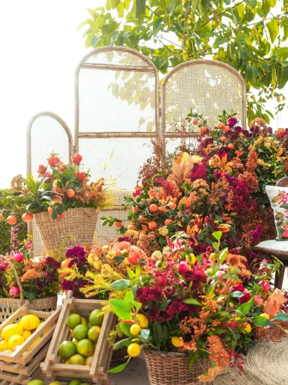 A vibrant and bountiful Haldi setup in Udaipur. The seating area is surrounded by an abundance of flowers in shades of red, orange, and yellow, with fresh lemons and limes in baskets adding a citrusy touch.