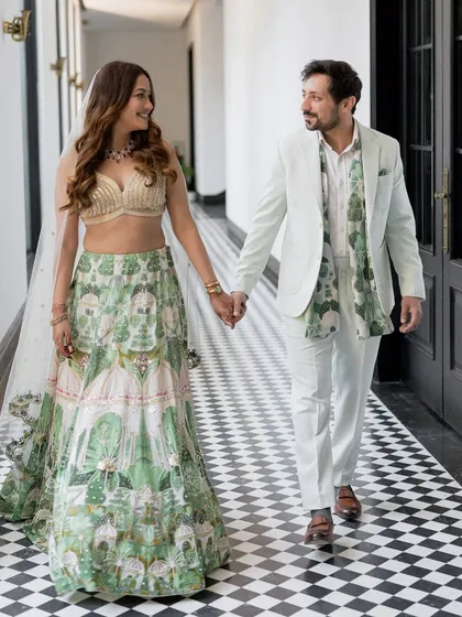 A stylish couple walking hand-in-hand at their Roka ceremony. Their coordinated green and white outfits are modern and chic.