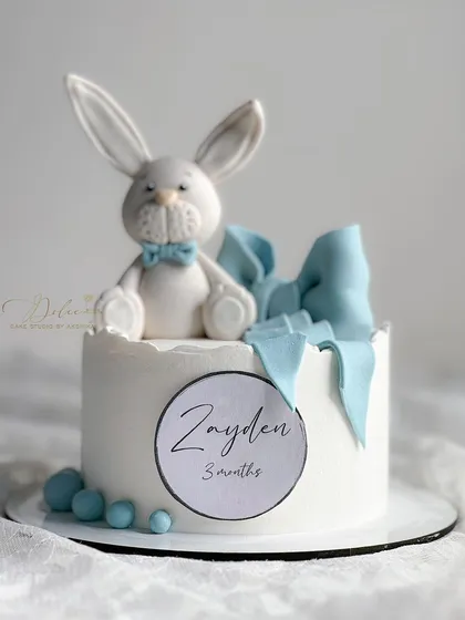 A clean and simple monthly milestone cake featuring an adorable, hand-sculpted bunny topper and a fondant bow.