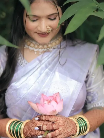 A close-up of the bride's hands holding a lotus flower, showcasing her intricate engagement mehndi. The design is as beautiful as the flower she holds.