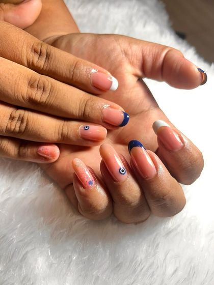 A chic and trendy design on natural nails. This set features a mix of white and navy blue French tips, with a couple of nails adorned with a delicate evil eye art.