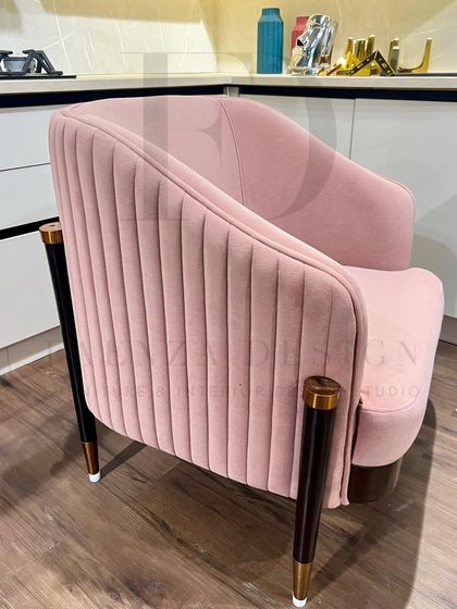 This armchair in a soft pink velvet features elegant vertical tufting on the back. The dark wooden legs with gold and copper-toned ferrules add a sophisticated, high-end detail.
