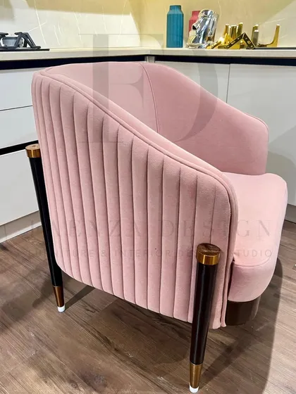 A pair of blush-pink armchairs with pleated backs and tapered legs with brass caps. These chairs are perfect for adding a touch of soft, modern glamour to a living room or kitchen seating area.