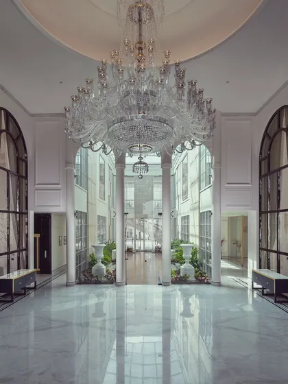 We believe a home's entrance should be a grand statement of what lies within. In this foyer for The Grand Alabaster, a magnificent crystal chandelier descends from a double-height ceiling, reflecting in the polished marble floors. This space was designed to create an unforgettable first impression of opulence and light.