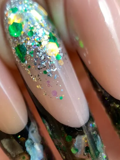 A close-up of an incredibly detailed aquarium-style nail extension, with green and silver glitter encapsulated within the clear tip.