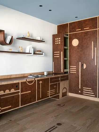 Storage should never be boring. For this multipurpose room, we designed a full-wall unit in rich burl veneer with intricate geometric inlays. The design combines different shutter types and playful motifs, with a surprise pop of mint green inside, turning a practical piece into a visual delight.