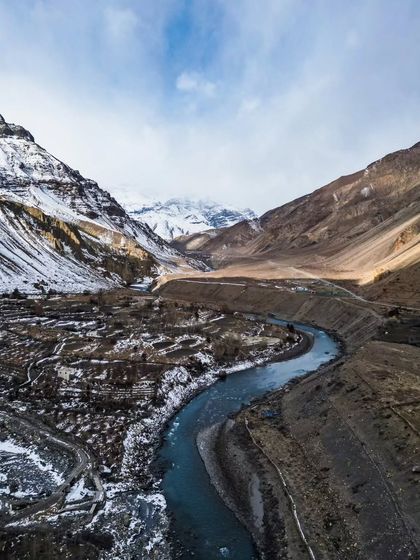 A drone shot capturing the winding Spiti River with snow-capped mountains in the background.