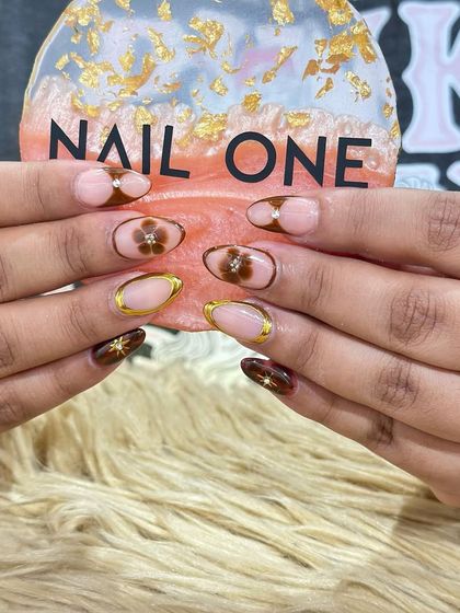 This sophisticated design combines earthy brown tones with delicate floral art. We used a sheer nude base and added gold chrome outlines and tiny rhinestones for a touch of elegance, making it perfect for festive occasions like Rakhi or Teej.