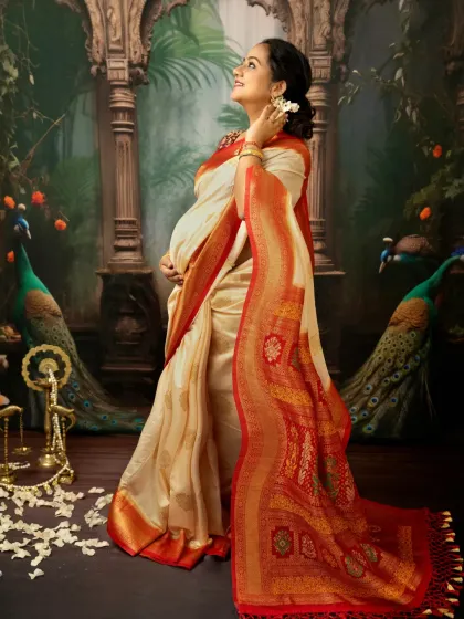A full-length portrait showcasing the splendor of a traditional Indian maternity look. The rich pallu of the silk saree, the delicate flower petals, and the regal pose against a painted backdrop create a truly majestic and memorable photograph.