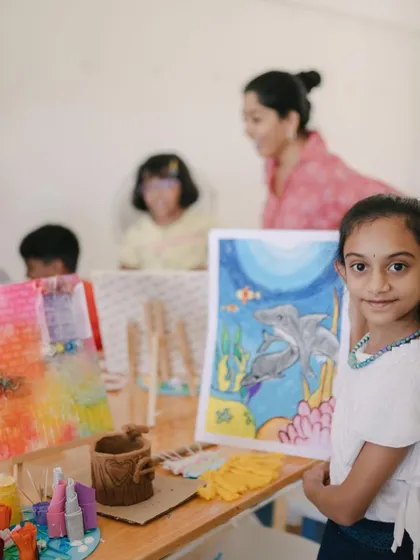 This young artist is standing proudly next to her work at our camp showcase. Her display includes a dolphin painting, a mixed-media canvas, and a 3D diorama, showing the variety of projects we tackle.