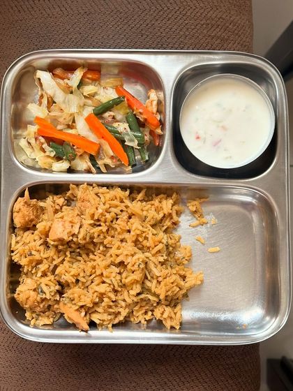 This plate features chicken biryani with a side of sautéed mixed vegetables and raita.