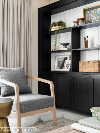 A mid-century modern armchair creates a cozy reading nook next to the window. The contrast between the black shelving and the white shiplap backing adds visual interest and a modern farmhouse touch.