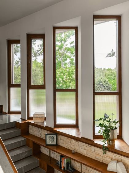 A series of tall, narrow windows offers curated views of the surrounding greenery. The lower panels use fluted glass to ensure privacy without sacrificing light, demonstrating a practical approach to window design.