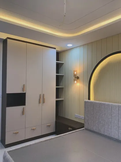 This bedroom design features a wardrobe with an integrated study or seating nook. The arched headboard with fluted paneling and backlighting creates a beautiful focal point in the room.