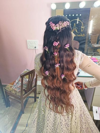 A whimsical half-up hairstyle with braids and waves, decorated with scattered pink flowers. This is a beautiful and romantic look for a Mehendi or Haldi ceremony.