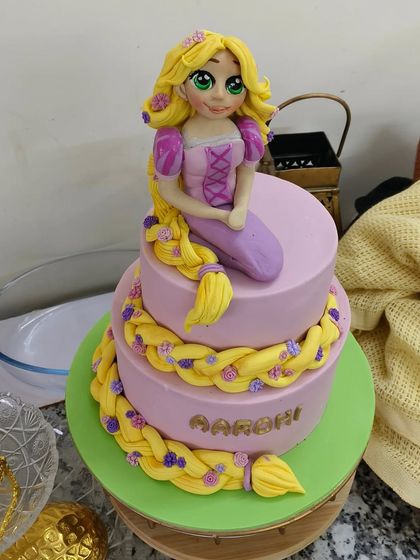 Rapunzel, Rapunzel, let down your long hair! This two-tiered cake features the beloved princess with her signature long, braided hair cascading down the sides. The entire piece, from Rapunzel herself to the tiny flowers in her hair, is completely handcrafted.