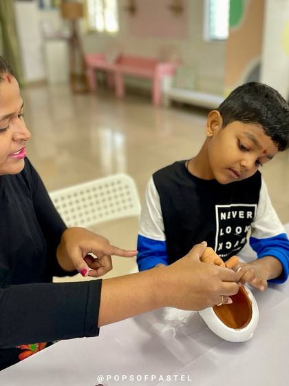 A mother guides her son as they begin painting a giraffe-shaped planter, a perfect bonding activity for our family workshops.