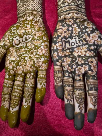 A close-up of the palms showing the fresh henna paste on one hand and the dark stain on the other, with the couple's names as the centerpiece.