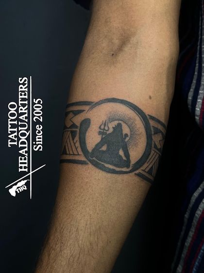 A creative armband tattoo featuring a silhouette of Lord Shiva meditating within a circle, blended with a tribal pattern.
