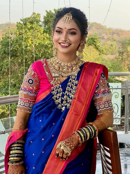 A vibrant blue and pink Paithani saree look, showcasing a traditional nath and layered gold necklaces.