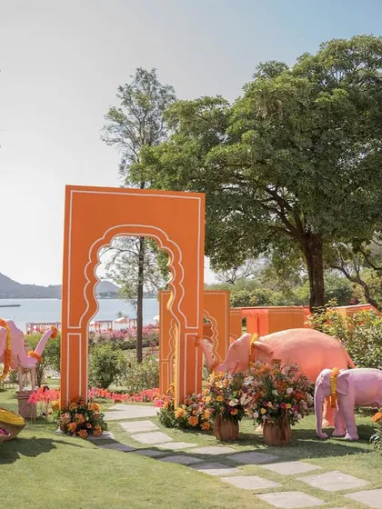 The vibrant entrance to a 'Pyaar ka Pind' Haldi ceremony in Udaipur. Whimsical pink elephants and bold orange arches welcome guests to a celebration filled with color, energy, and a modern take on Punjabi traditions.
