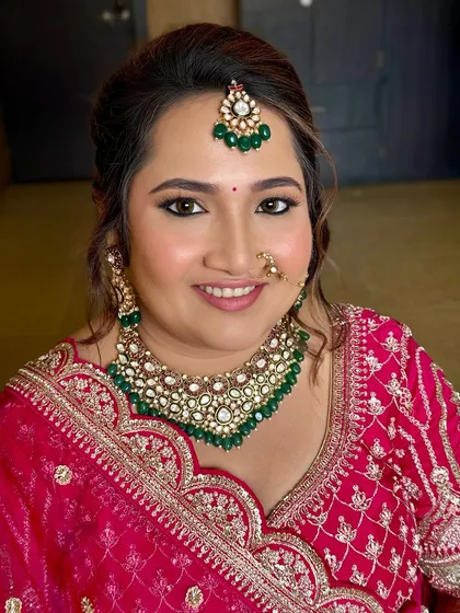 This bridal portrait showcases a flawless base with soft contouring and a defined eye. The look is designed to enhance the bride's features and complement her stunning pink and green ensemble.