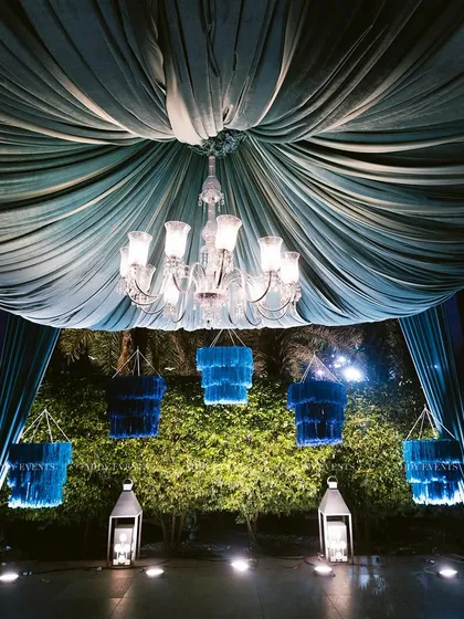 A beautiful stage setup with a royal blue canopy and hanging chandeliers. This design is perfect for an intimate yet grand welcome lounge or a sophisticated cocktail evening.