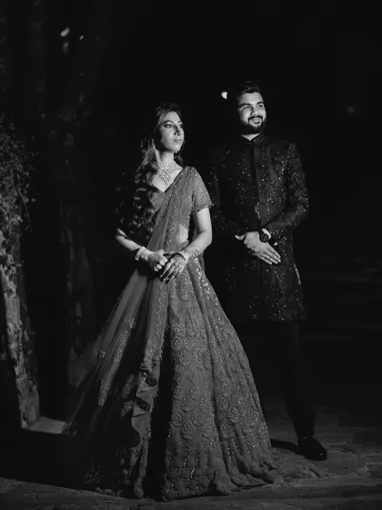 A dramatic black and white portrait of the couple at night. The low-key lighting creates a moody and romantic atmosphere, highlighting their elegant attire.