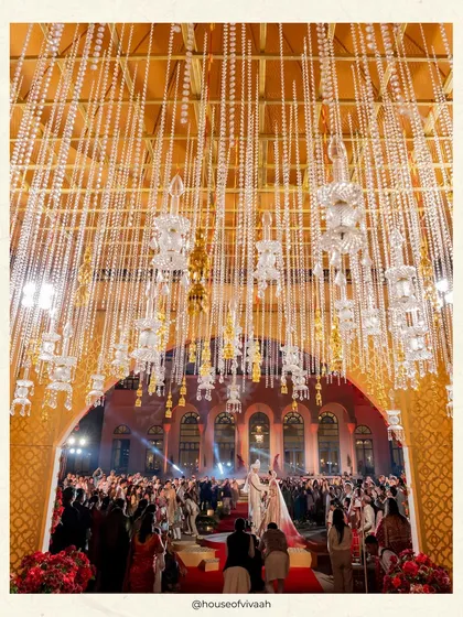 A view from inside the mandap looking out, showing the intricate ceiling of suspended pearl strings and crystal kaliras, creating a shimmering canopy for the couple.