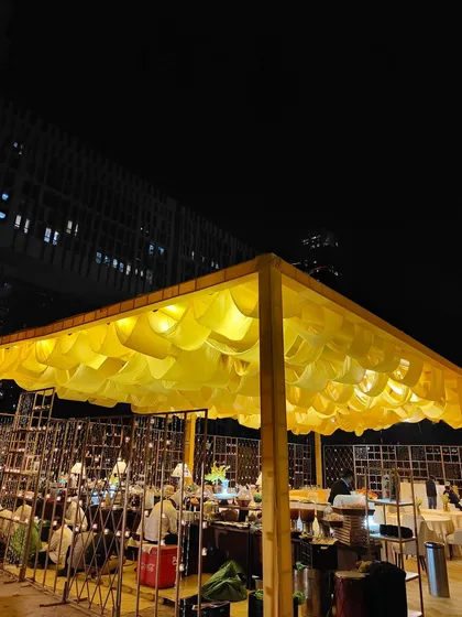 An outdoor food station setup under a canopy of draped yellow fabric, creating a festive market feel. I design catering areas to be an integral part of the event's aesthetic.