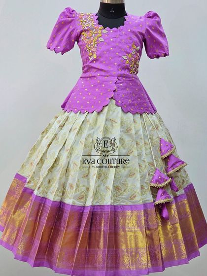 A beautiful Kanchi Pattu lehenga in lavender and off-white. The blouse has an asymmetrical peplum design with floral embroidery.