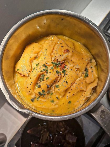 A pot of freshly cooked agnolotti, tossed in a creamy, vibrant yellow sauce and finished with fresh herbs. This is comfort food elevated to a fine dining standard.