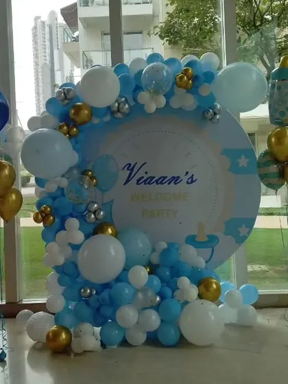 A classic and elegant welcome party setup for baby Vian. This decoration features a personalized circular backdrop with a blue, white, and gold organic balloon garland, perfect for celebrating the arrival of a newborn boy.