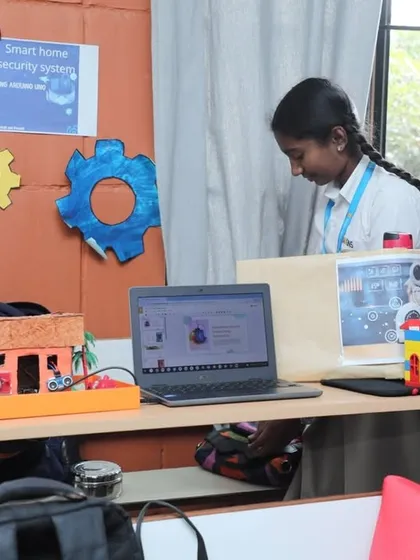 A student presents her "Smart Home Security System" project. This model demonstrates how sensors and coding can be used to create an automated security setup, reflecting the practical applications of IoT we teach.