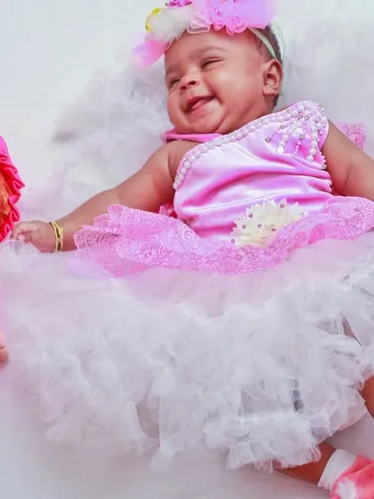 A delightful themed baby photoshoot with a baby girl in a frilly pink dress lying next to a matching doll. We use creative props and outfits to create fun and memorable portraits.
