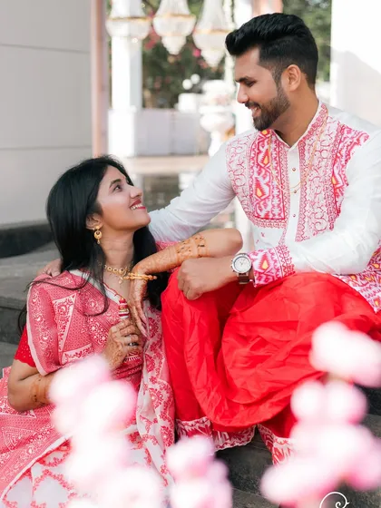 A romantic portrait of a Bengali couple, framed by pink flowers.