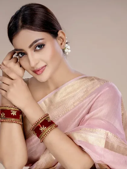This image highlights a set of rich red bangles against a soft pink saree. The color contrast and elegant pose make it a strong visual for lookbooks and online stores.