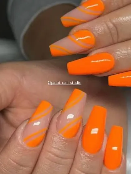 A bold and graphic summer look. This design features bright, solid orange nails paired with accent nails that have orange swirls on a clear base.
