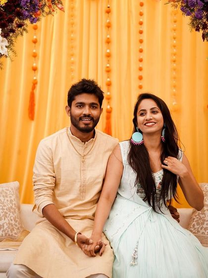 A happy couple at their Mehendi ceremony. We created a colorful and comfortable seating area with a bright yellow backdrop and a floral arch decorated with multi-colored flowers.