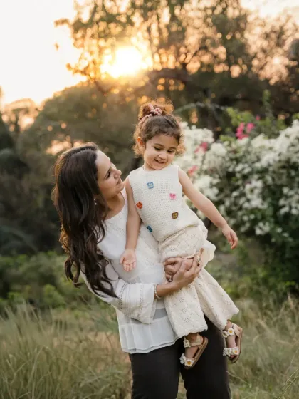 A mother holds her daughter against the warm glow of the setting sun. This outdoor portrait is filled with warmth and affection.