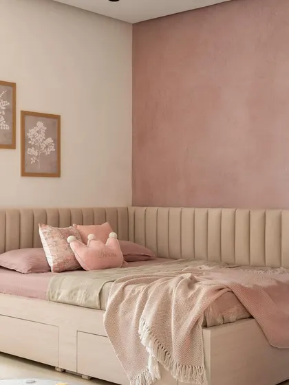 The cozy corner bed in the kids' room features a channel-tufted, wrap-around headboard in a soft beige. The walls are painted in a textured pink, creating a warm and comforting sanctuary.