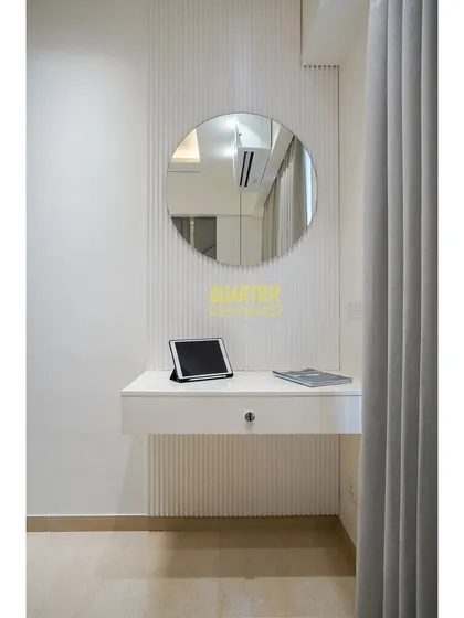 This guest bedroom includes a minimalist floating dressing table with a large round mirror. The wall behind features vertical fluting, adding texture and interest to a simple, functional corner.