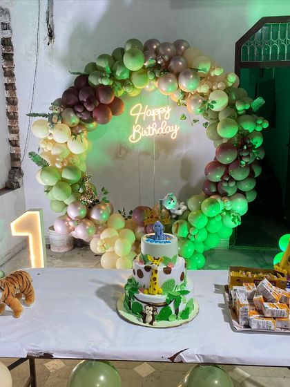 A close-up of the jungle-themed cake placed in front of the circular balloon arch and neon sign.