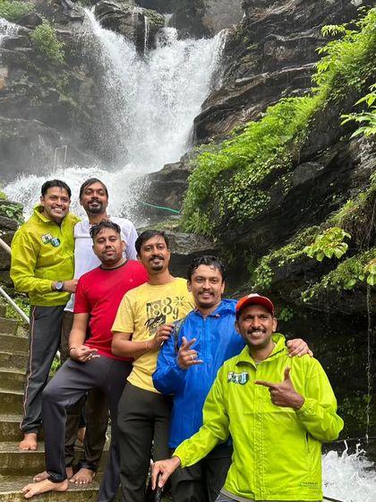 A group of friends posing on the steps near a waterfall, enjoying their monsoon adventure.