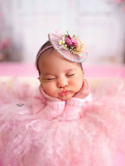 That perfect little pout! This close-up shot captures the adorable details of a sleeping newborn, from her puckered lips to her tiny hands, all while she dreams away in a fluffy pink setup.