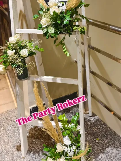 A rustic decorative ladder adorned with bouquets of white flowers and dried pampas grass, adding a charming touch to a terrace party entrance.