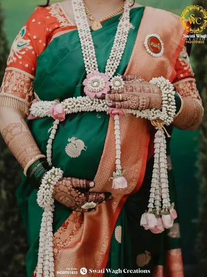A close-up of the floral kamarband, a beautiful way to adorn the baby bump. The 'Aai' brooch is a special, customized touch.