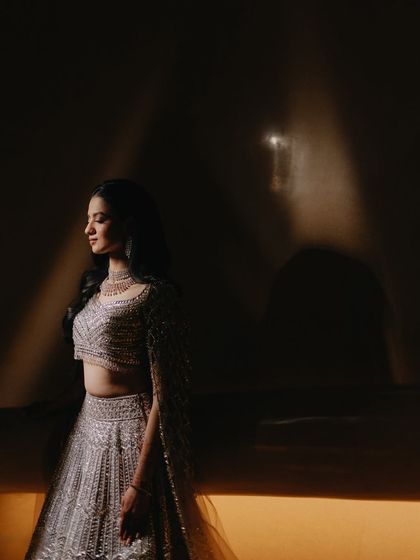 A beautiful bridal portrait using light and shadow. The dramatic lighting sculpts her features and highlights the intricate details of her lehenga, creating a moody and artistic solo shot.