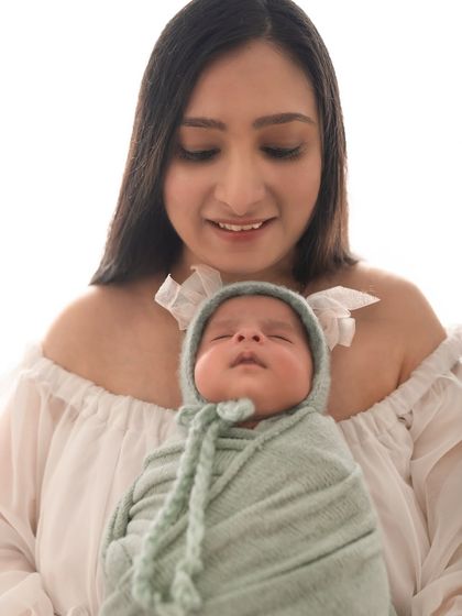 A close-up portrait of a mother admiring her newborn. The soft lighting and simple background keep the focus entirely on the emotion.